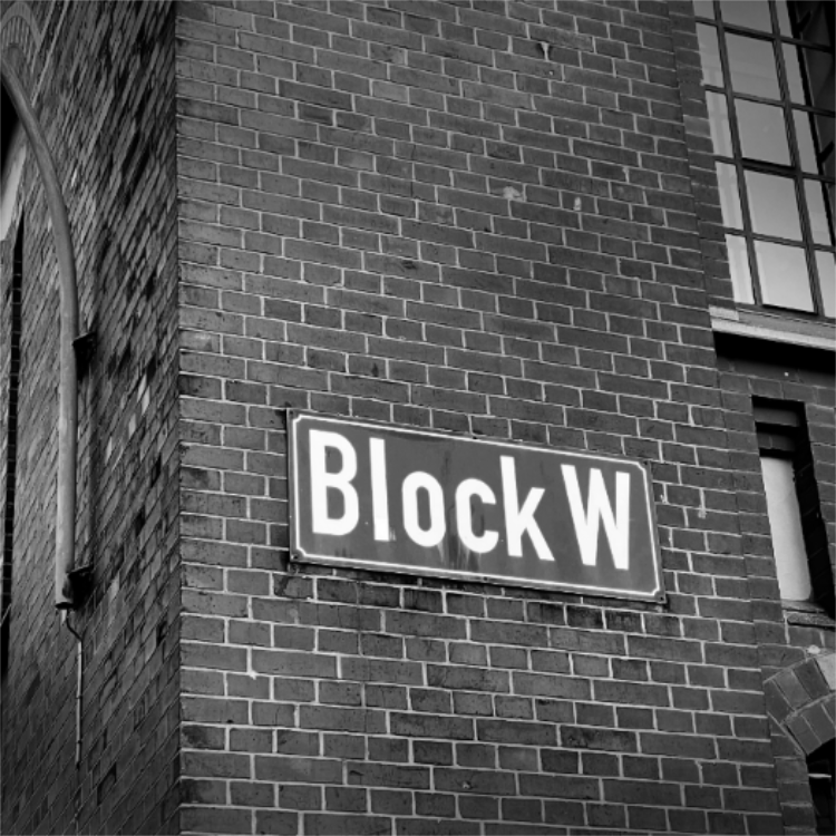 Showing the block w sign with white letters on green ground on a red brick wall of the historic building the studio is located in.